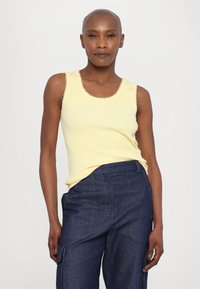 Helles gelbes, geripptes Tanktop mit gewellten Kanten, kombiniert mit dunkelblauen Cargo-Jeanshosen mit Taschen und kontrastierenden Nähten.