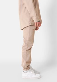 Beige cargobroek met zijzakken, elastische boorden en een relaxte pasvorm, gecombineerd met witte sneakers. Gladde stofstructuur.