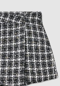 Jupe en tissu tissé noir et blanc avec un motif à carreaux texturé et des accents dorés, présentant un design plissé.