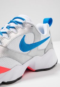 Les chaussures de sport Nike présentent un upper en maille argentée avec des accents bleus, une semelle intermédiaire blanche rembourrée et une touche de rose au niveau du talon. Semelle en caoutchouc noire.