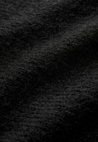Zwart textiel met een zachte, donzige uitstraling, met variërende dieptes en subtiele vezels door het oppervlak.