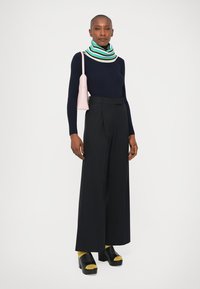 Ναυτικό ριγωτό πουλόβερ, ριγωτό κασκόλ, ψηλόμεσες μαύρες πλισέ παντελόνες, κάλτσες με κίτρινες λεπτομέρειες, μαύρες πλατφόρμες. Ροζ τσάντα.