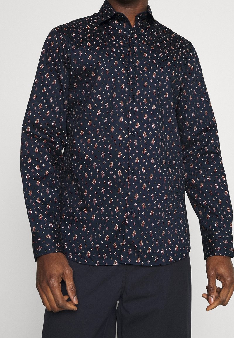 Marinblå skjorta med knappar och små blommönster i rött och vitt. Har en klassisk krage och långa ärmar. Slät tygtextur.