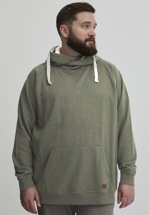 Sudadera con capucha de color verde oliva, con un bolsillo frontal, tejido texturizado y cordones crema. Presenta una etiqueta en la parte inferior derecha.