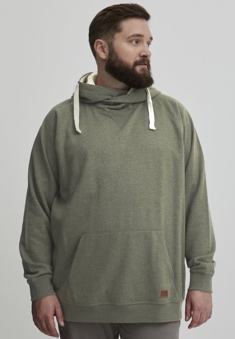 Sudadera con capucha de color verde oliva, con un bolsillo frontal, tejido texturizado y cordones crema. Presenta una etiqueta en la parte inferior derecha.