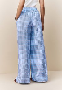 Modre in bele široke hlače iz ginghama imajo teksturirano tkanino, elastičen pas in stranske žepe. Rob hlačnic je nad stopali.