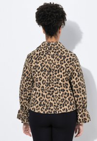 Jaguarprickig jacka med krage, långa ärmar med volangärmar och ryggveck. Strukturväv i beige och svart.