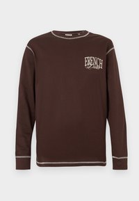 Καφέ μακρυμάνικη μπλούζα με στρογγυλή λαιμόκοψη, με λευκές ραφές σε αντίθεση και το γράφημα "FRENCH DINER" στο αριστερό στήθος.