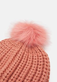 Kötött sapka poros rózsaszínben, amelynek tetején egy bolyhos pink pom-pom található. A texturált fonal bordázott mintázatot mutat.