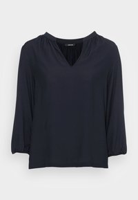 Blouse bleu marine en tissu doux avec un décolleté en V, des manches bouffantes 3/4 et une coupe décontractée, présentant de légères fronces aux épaules.
