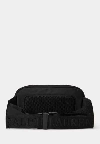 Melna jostas soma ar sieta priekšējo kabatu un regulējamu siksnu ar izspiestu "Ralph Lauren" logotipu, attēlota uz baltas fona.