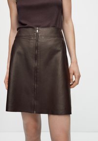 Gonna in pelle marrone con una superficie liscia, caratterizzata da una chiusura con zip frontale e vita aderente. Design semplice senza fantasie o dettagli.