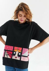 Černé oversized tričko s barevným, kresleným lemem s růžovými, červenými a černými akcenty, včetně grafiky postav.