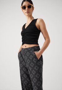 Svart ribbet crop topp med v-hals og rynket detalj foran, kombinert med løse svarte bukser med et hvitt geometrisk mønster.