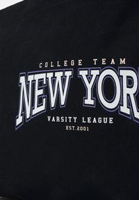 Tissu noir avec texte blanc et violet affichant "College Team New York Varsity League Est. 2001" en police style varsity.