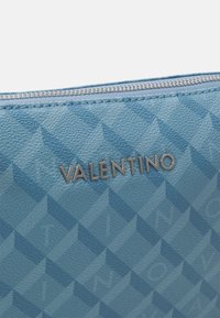 Světle modrá kožená taštička s texturou a geometrickým vzorem, s stříbrným logem 'VALENTINO' na přední straně a stříbrným zipem.