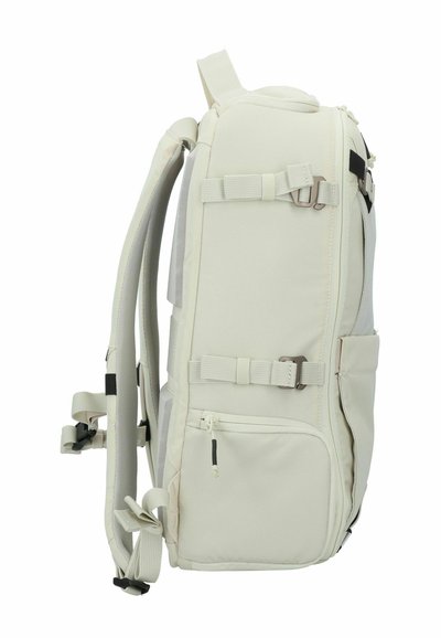 Mochila beige con un exterior de nailon texturizado, múltiples correas ajustables, cremalleras y bolsillos laterales para almacenamiento. Diseño duradero y espacioso.