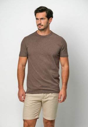 Maglietta marrone a maniche corte realizzata in un tessuto morbido e dalla texture irregolare; abbinata a pantaloncini beige chiaro. Girocollo semplice senza motivi visibili.