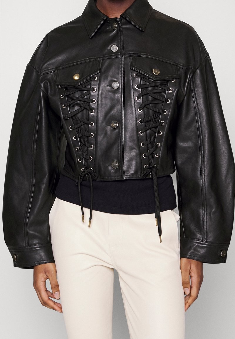 Svart skinnjacka i kort modell med knäppning framtill, snörningsdetaljer och bronsfärgade metalldelar, med ett svart elastiskt midjeband.