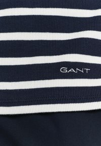 Marineblå og hvidstribet bomuldsstriktrøje med ribbet struktur; "GANT"-logo broderet i hvidt på kanten.