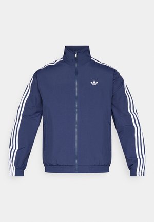 Μπλε ναυτικό μπουφάν με φερμουάρ, ψηλό γιακά, λευκές τρεις ρίγες στα μανίκια και κεντημένο λογότυπο στο στήθος. Ελαφρύ υλικό.