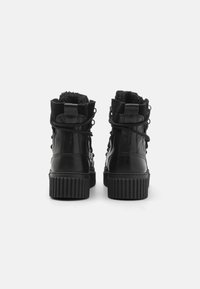 Botoșei negri până la gleznă, din piele lucioasă, cu tălpi din cauciuc texturat, având design cu șireturi și căptușeală din blană artificială în partea de sus.