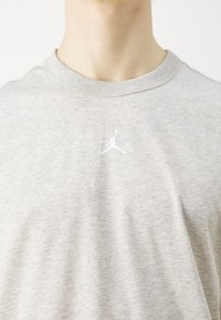 Šedé bavlněné tričko s kulatým výstřihem a krátkými rukávy. Obsahuje malé bílé logo Air Jordan na hrudi. Měkká textura.