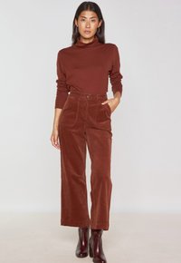 Top a collo alto marrone abbinato a pantaloni in corduroy a gamba larga e alta vita. Presenta tasche frontali e chiusura con bottone. Tessuto liscio.