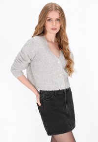 Hellgraue Strick-Cardigan mit tiefem V-Ausschnitt, kurzen Ärmeln und fünf Knöpfen, kombiniert mit einem schwarzen Jeans-Minirock.