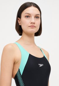 Μαύρο μαγιό με τιρκουάζ μπλε λεπτομέρειες και ζικ ζακ μοτίβο στο πλάι. Σχεδιασμένο με λεπτές τιράντες και προσιτό ντεκολτέ. Εμφανές το λογότυπο της μάρκας.