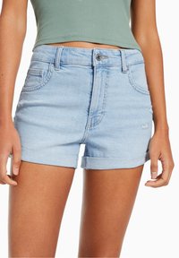 Shorts de mezclilla de lavado claro con dobladillos enrollados, que presentan bolsillos frontales y una cinturilla ajustada con un cierre de botón metálico. Textura suave.