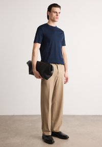 Jūros laivyno trumpomis rankovėmis marškinėliai su tekstūruotu raštu, derinami su smėlio spalvos plačiakojėmis kelnių ir juoda sulankstoma rankine, dėvimi su juodais batais.