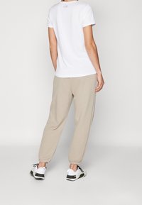 Weißes Kurzarmhemd mit Logo, beigefarbene tapered Sweatpants und graue Sportschuhe mit schwarzen und gelben Akzenten. Einfaches, lässiges Outfit.