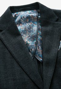 Blazer en laine à chevrons foncés avec une doublure en satin à motif paisley en bleu, teal et cuivre. Présente un col cranté et une poche.