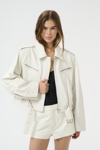 White leather cropped jacket with shoulder epaulettes, two zippered front pockets, and belted detail. Paired with white leather shorts.