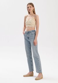 Jasno beżowy krótki top z kwiatowym wzorem, zestawiony z jasnoniebieskimi, wysokimi dżinsami i beżowymi butami na koturnie. Prosty, prosty krój.