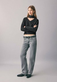 Svart cropped tröja med V-ringning och metalliska detaljer, i kombination med ljusgrå jeans med dekorativa inslag och svarta ankelstövlar.