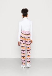 Top branco de mangas longas combinado com calças de cintura alta com um padrão zigzag multicolorido em tons de rosa, laranja e castanho.