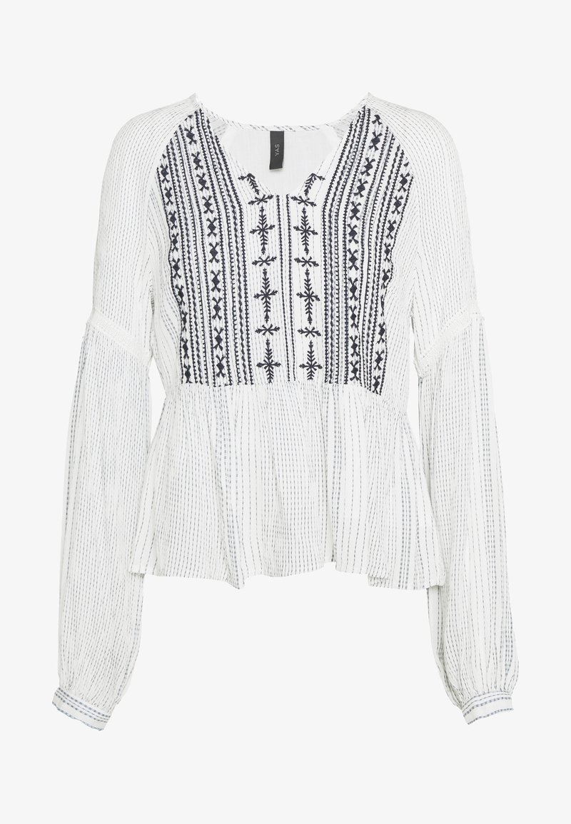 Blouse blanche à manches longues avec rayures verticales noires, broderie noire complexe sur la poitrine, coupe ample avec un léger bas volanté et poignets froncés.