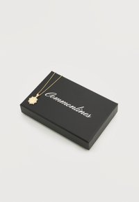 Χρυσό κολιέ με μενταγιόν σε σχήμα ήλιου με λεπτομέρειες στο κέντρο, σε λεπτή αλυσίδα, τοποθετημένο πάνω σε μαύρο ορθογώνιο κουτί με την επιγραφή "Commonlines".