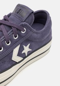 Fioletowe zamszowe trampki Converse All Star z białym logo gwiazdy i białą gumową podeszwą z czarnymi paskami.