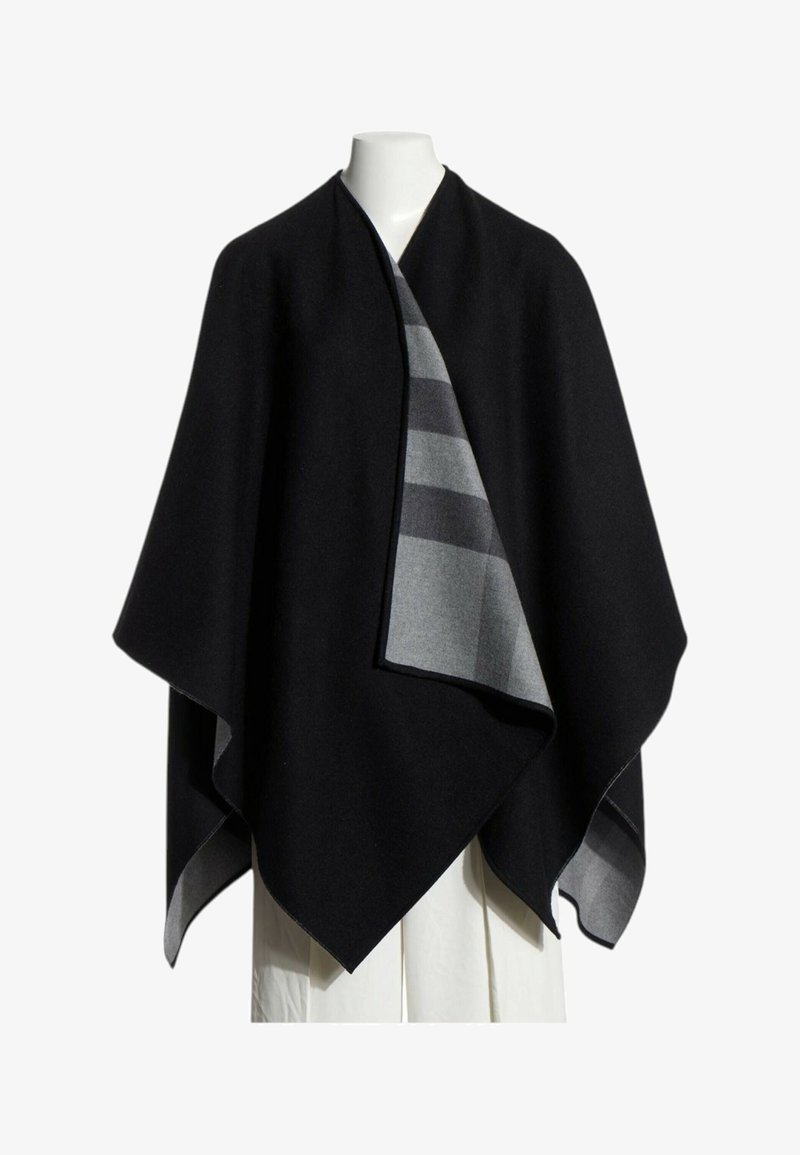 Cape noire style enveloppe avec doublure rayée grise, présentée sur un mannequin blanc sur fond uni.