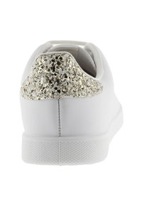 Baskets blanches avec une semelle extérieure en caoutchouc texturé, un dessus lisse, et une section pailletée dorée et noire sur le talon.