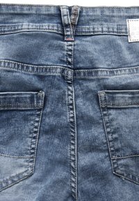 Jean en denim bleu moyen avec un léger effet usé. Il possède deux poches arrière, des coutures visibles et une étiquette sur la taille.