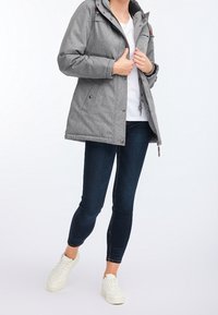 Harmaa eristetty takki hupulla, jossa on vetoketju- ja nappisulku, sivutaskut sekä ruskeat nahka-akcentit. Päällä valkoinen t-paita.