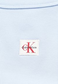 Light blue ribbed fabric with a white label featuring red "CK" and "Calvin Klein" text. Focus on texture and logo detail.