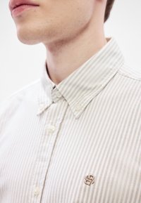 Ριγέ πουκάμισο με κουμπιά σε μπεζ και άσπρο, με γιακά, υφασμάτινη υφή και κεντημένο λογότυπο στο στήθος.