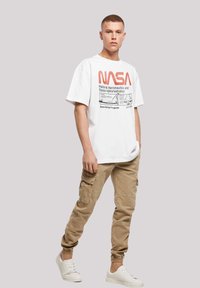 White t-shirt with red NASA graphic print, casual fit, paired with beige cargo pants featuring pockets and elastic cuffs, worn with white sneakers.