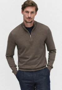 Brun zip-up tröja i mjukt tyg; har en hög krage och ribbade ärmslut, bärs över en marinblå skjorta och matchas med mörka byxor.