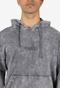 Sudadera con capucha gris hecha de tela suave, con bolsillo canguro, capucha con cordón y el logo cosido "THE JOKERS" en el frente.